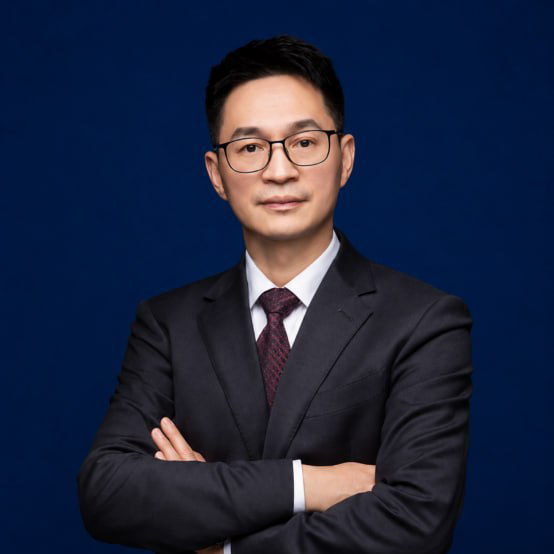 Professional man in suit with curly hair smiles in a corporate setting, blurred office background.